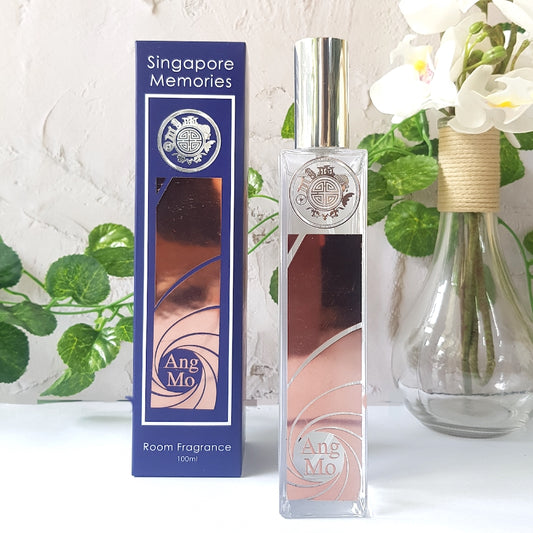 Elegant ‘Singapore Memories’ room fragrance named ‘Ang Mo’ in a tall, slender bottle with a spray nozzle, set against a blue backdrop featuring architectural elements and the brand’s crest.