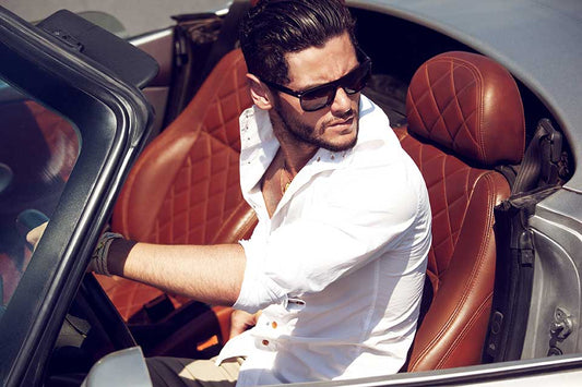 Man sitting in a luxury car with open top, wearing sunglasses and a white shirt.