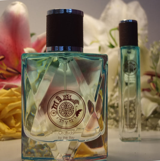 orchids by the bay perfume bottle large 100ml in the foreground and travel size 18ml in the background with yellow flowers and orchids