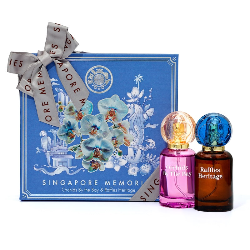 A perfume dual gift set from Singapore Memories, featuring a blue box with floral designs and two perfume bottles, one with a pink label and the other with a brown tinted bottle both having blue caps.