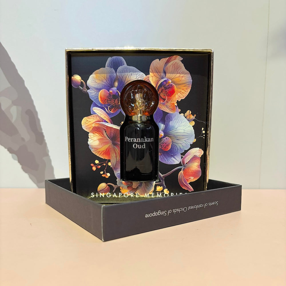 A bottle of Peranakan Oud perfume displayed in front of a box with floral artwork. The packaging includes the text 'Peranakan Oud' and 'Singapore Memories'.