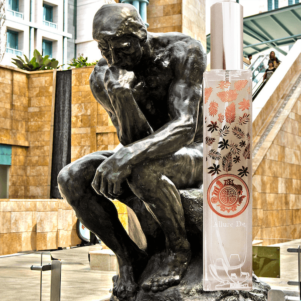A bronze sculpture of ‘The Thinker’ by Auguste Rodin, placed next to a tall white cylindrical object adorned with floral patterns and text. The juxtaposition of classical art and modern advertising creates an intriguing contrast.
