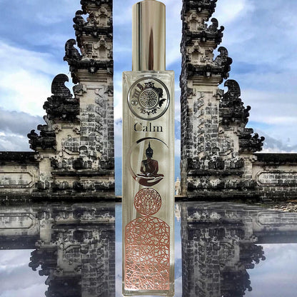 A bottle of fragrance labeled 'Calm' standing in front of an ancient stone gate with intricate carvings, reflecting in water below.