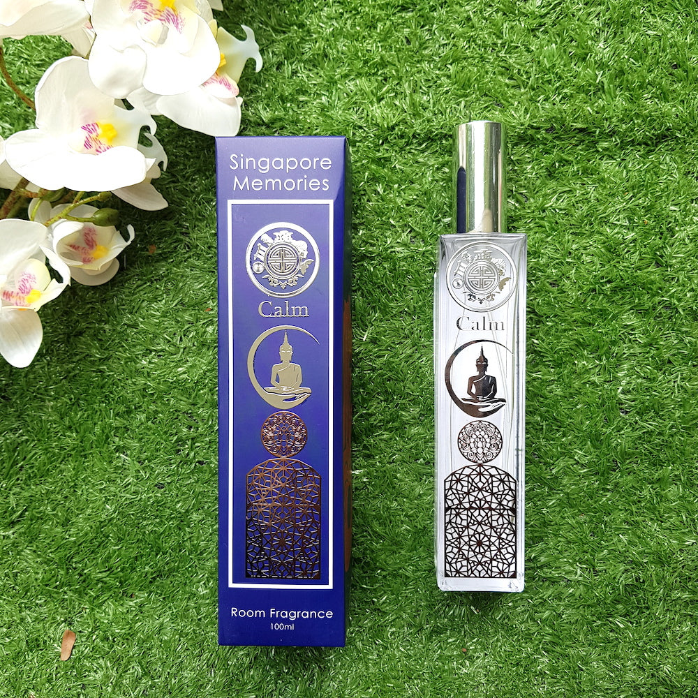 calm scent bottle with buddha and other relaxing symbols next to a blue gift box on top of green grass and orchids