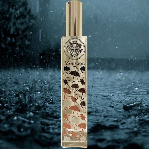 A bottle of Monsoon fragrance with a gold cap, set against a rainy window background.