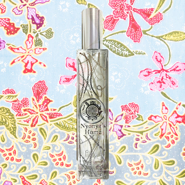 A bottle of Nyonya's Home fragrance with silver chain decoration with a floral pattern in the background that is inspired by singapore batik
