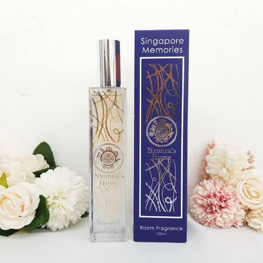 Nyonya room scent fragrance by singapore memories in a crystal bottle next to a blue gift box with silver chain decoration and in front of white florals