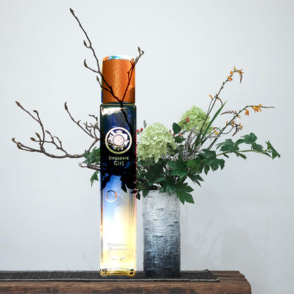 Singapore girl perfume in blue bottle with white background, next to a flower pot with ferns
