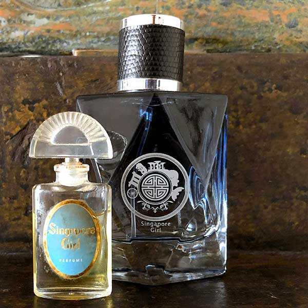 Two perfume bottles, one new blue large and one older small, for singapore girl on a textured surface with a blurred background.