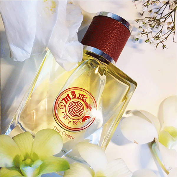 Perfume bottle with a red cap and visible brand logo, surrounded by flowers on a light background