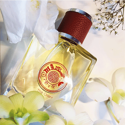 Perfume bottle with a red cap and visible brand logo, surrounded by flowers on a light background