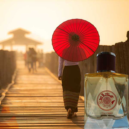 Person holding a red umbrella on a wooden boardwalk with a bottle of perfume in the foreground called 'the orient' by singapore memories 