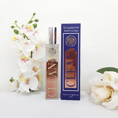 CLEAN room fragrance by singapore memories in a glass and metal bottle next to a blue gift box, in front of white background, surrounded by white orchids and rose