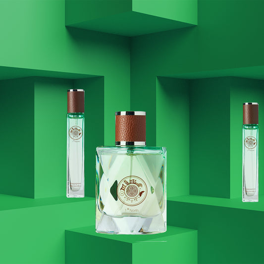 Three bottles of 'One Degree North' perfume positioned against a green, solid-patterned background. The bottles are transparent with a leather-look cap, displaying the perfume's colorful liquid inside.