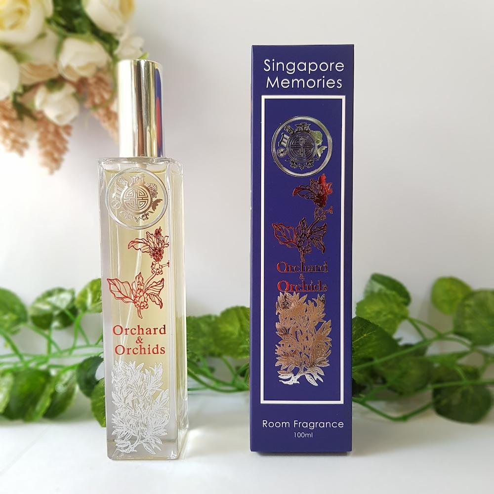 Orchard and orchids room fragrance in crystal bottle with special floral motif next to a blue corporate gift box with red and silver metal design and a shiny circle singapore memories logo