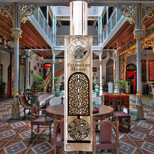 A tall, ornate bottle of Peranakan fragrance, with intricate carvings and designs, displayed in a beautifully decorated room.