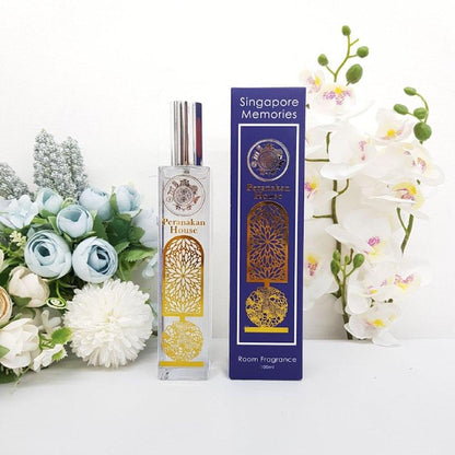 Peranakan house room fragrance in a glass and gold bottle next to a blue gift box, surrounded by white orchids 7 other flowers.