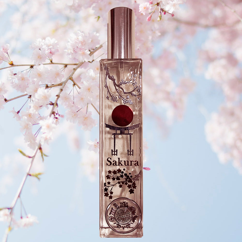 A clear glass bottle with a silver cap and a red spherical object inside, labeled 'SAKURA', set against a background of pink cherry blossoms.