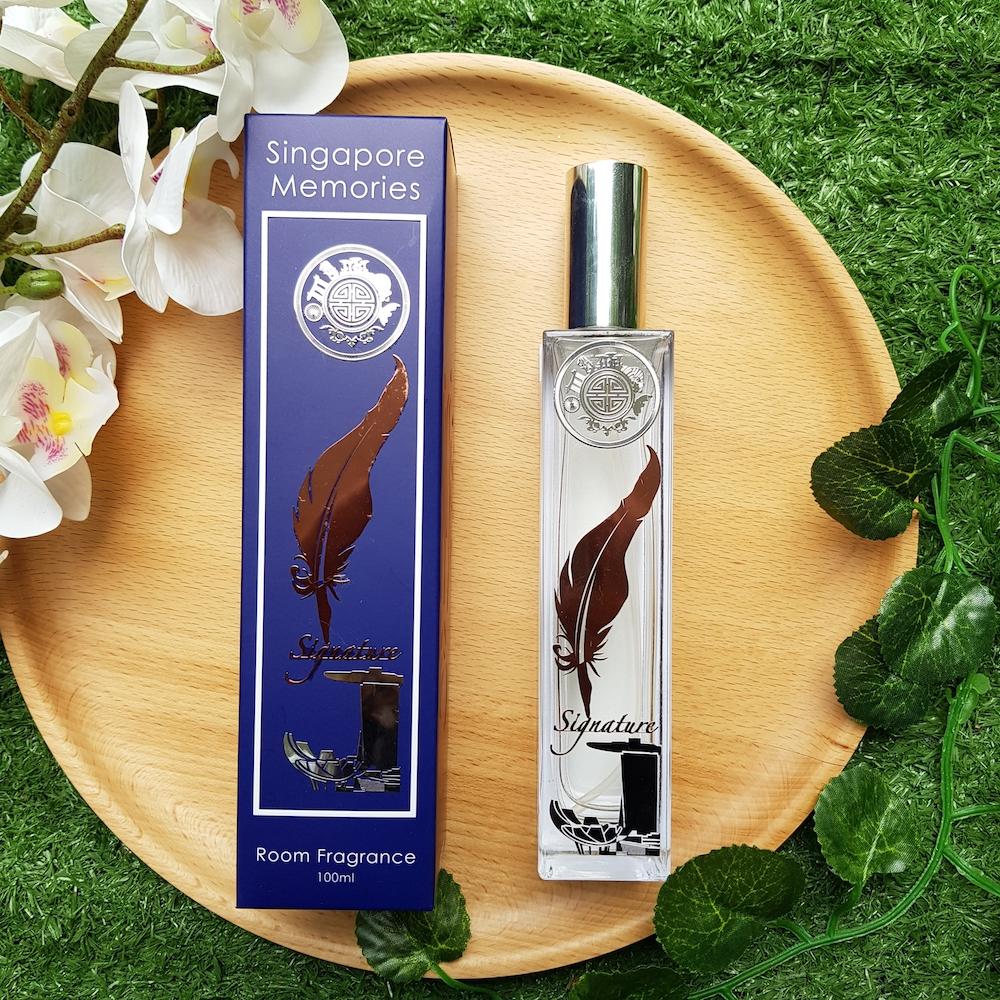 Signature singaporememories room fragrance in glass bottle next to blue gift box and on top if a wooden circle