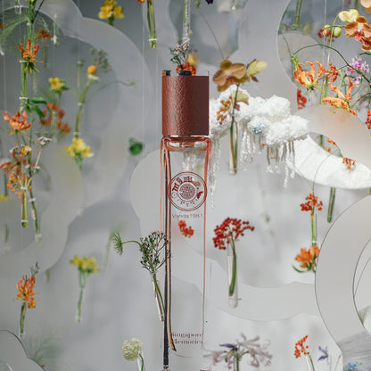 A bottle of Vanda 1981 perfume in a clear glass with a copper-colored cap, set against a floral-themed backdrop with various orchids and flowers.